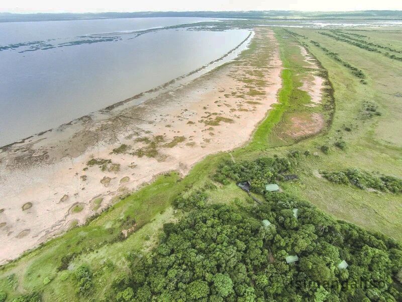 Aerial view of the lake shore, with lodge roofs tucked into the forest above the sand flats