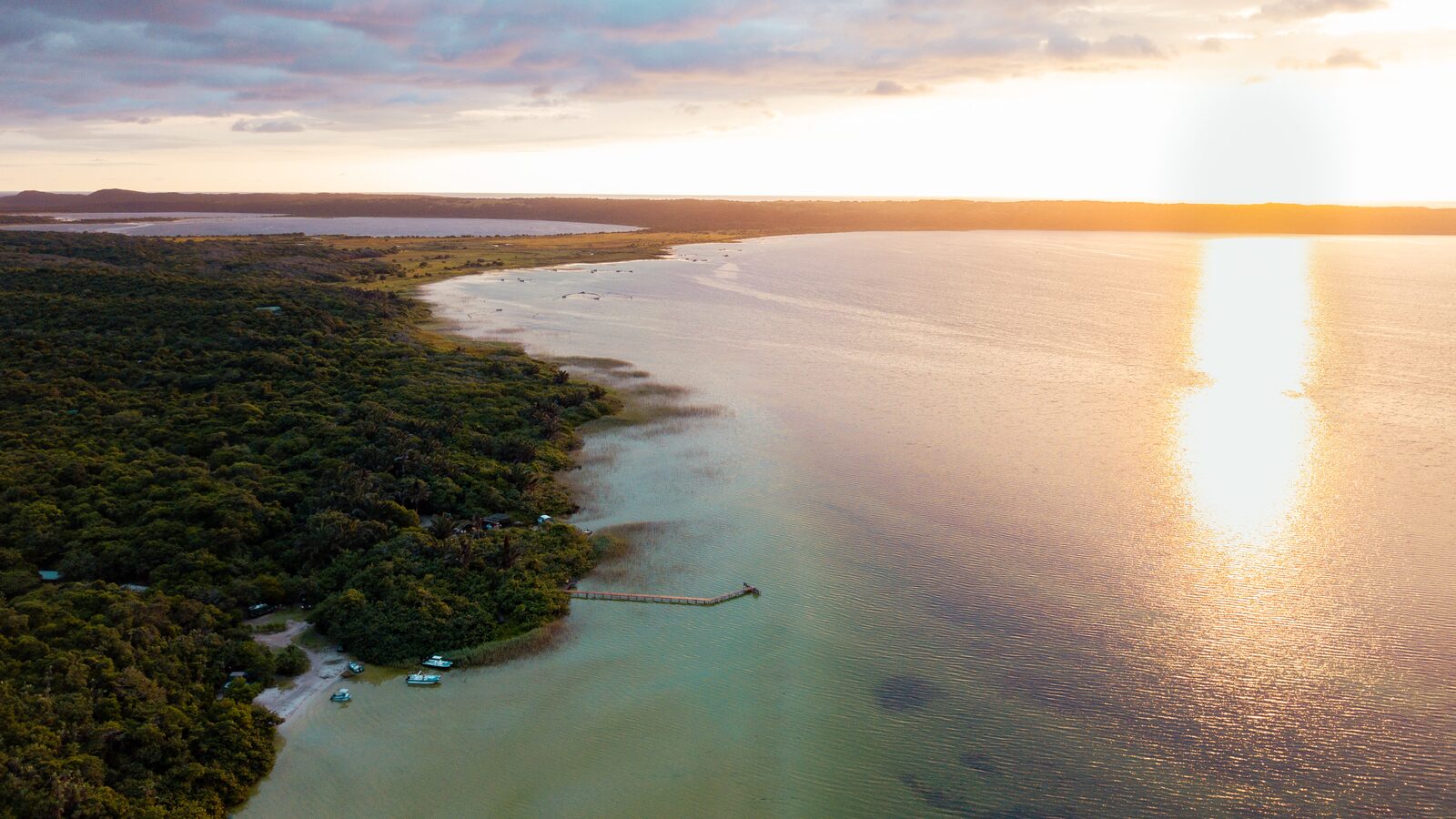 Aerial view of the Kosi Bay lake system at sunset, with boats and fish kraals along the forested shore